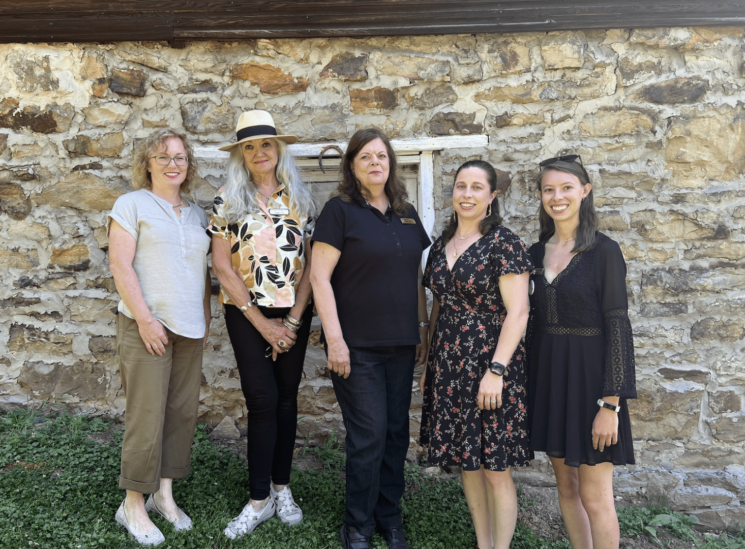 Five women stand in front of a stone wall.